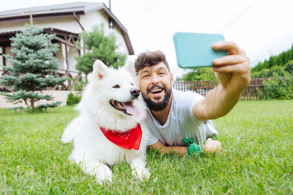 Beaming handsome man making selfie with his white husky