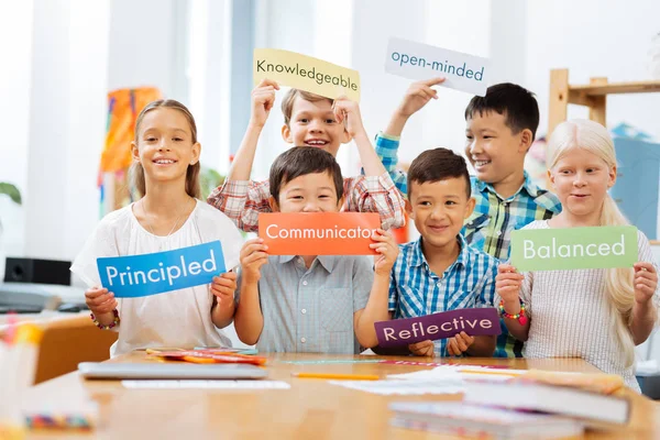 Smilende skolebørn stående midt i et klasseværelse - Stock-foto