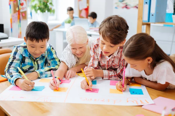 Vrolijke kinderen tekenen van een poster in een klaslokaal — Stockfoto