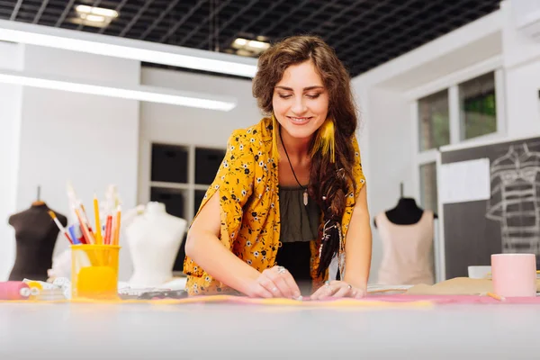 Costureira alegre sorrindo enquanto desenha linhas no tecido — Fotografia de Stock