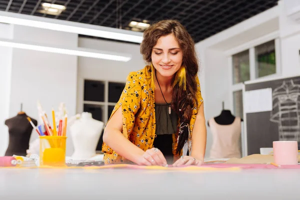 Joyeux couturière souriant tout en dessinant des lignes sur le tissu — Photo