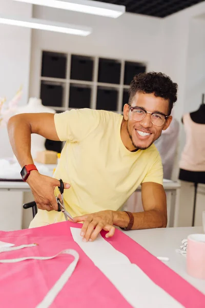 Atrakcyjne młody człowiek uśmiechający się szczęśliwie podczas cięcia różowa tkanina — Zdjęcie stockowe