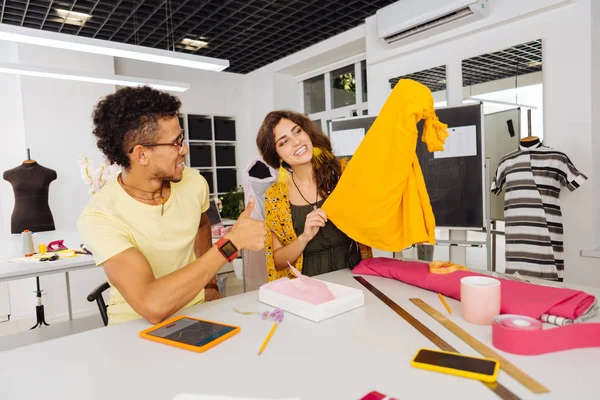 Happy dressmaker showing blouse to her colleague and looking happy — Stock Photo, Image