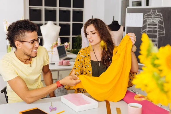 Skilled dressmakers discussing the textile while touching yellow blouse — Stock Photo, Image