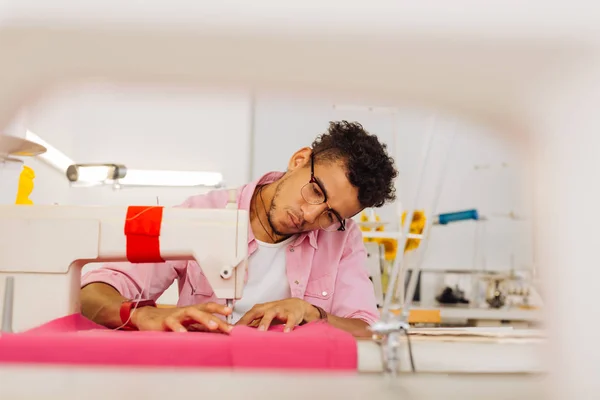 Ernstige jonge man leunt zijn hoofd tijdens het gebruik van de naaimachine — Stockfoto