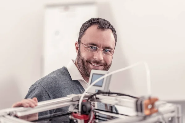 Hombre agradable en gafas sentado cerca de la impresora 3D — Foto de Stock