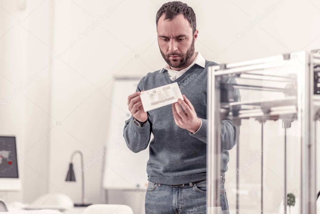 Concentrated adult man holding a detail of 3d printer