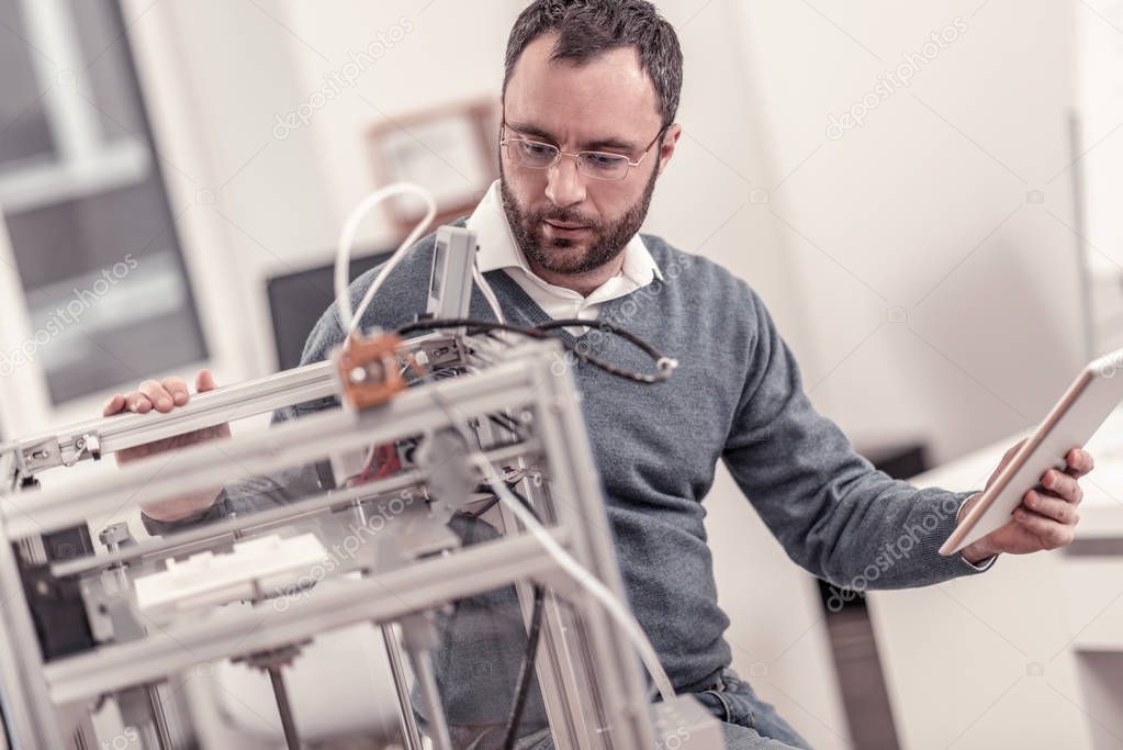 Bearded adult man adjusting 3D printers components