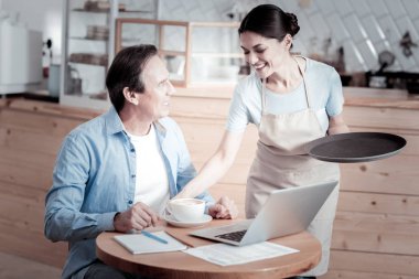 Kahve masanın üzerine koyarak ve gülümseyen profesyonel garson