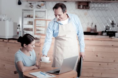 Bir dizüstü bilgisayar ve kahvesini getiren garson çalışan mutlu kadın
