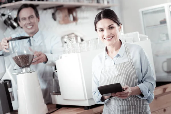 Holding bir hesap makinesi ve kahve yapma bir barista garson gülümseyerek — Stok fotoğraf