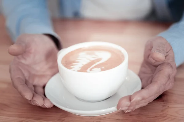 Руки человека, прикасающегося к чашке и показывающего искусство латте — стоковое фото
