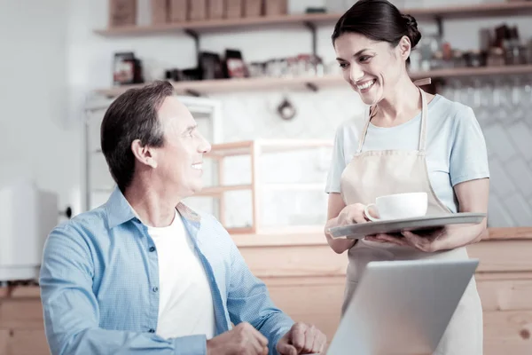 Smiling waitress holding coffee on a tray and looking at the visitor — Stock Photo, Image