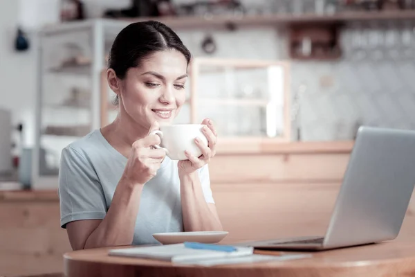 Спокойная женщина, чувствующая запах кофе, сидя за столом — стоковое фото