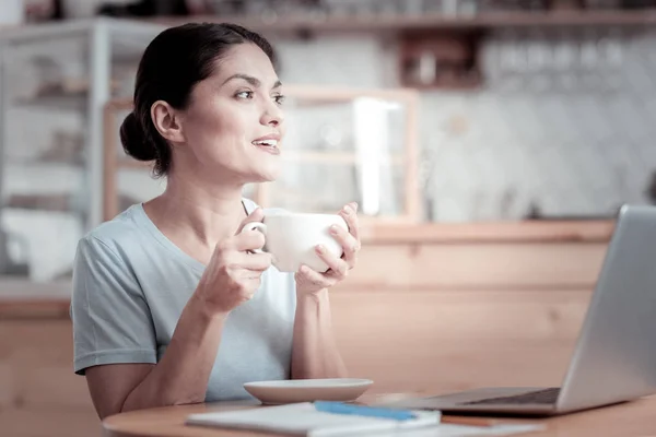 Femme souriante regardant au loin tout en buvant du café dans un café — Photo