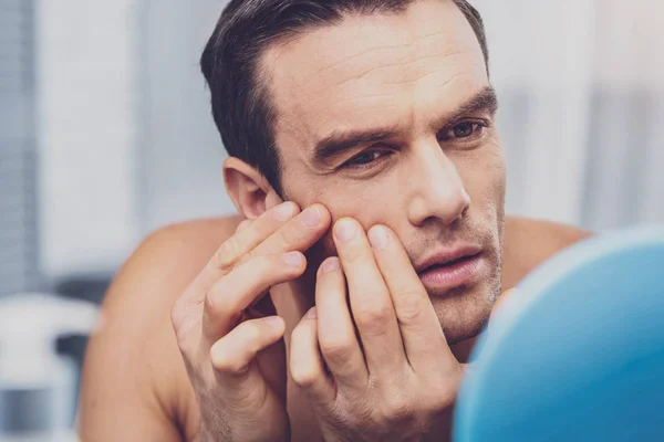 Schöner Mann, der sein Gesicht berührt, während er in den Spiegel schaut — Stockfoto