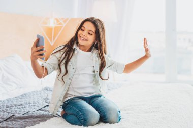 Kıvırcık kız çift kişilik yatak üzerinde otururken selfie yapma