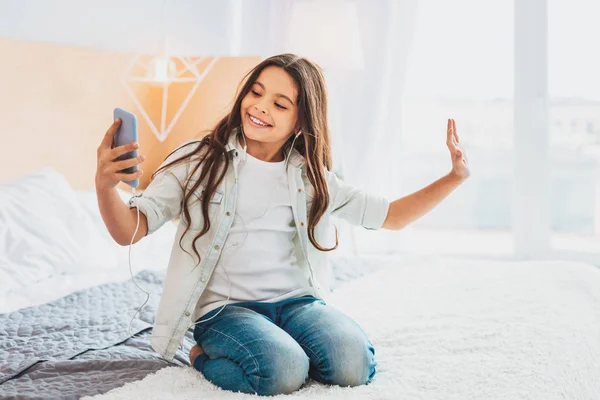 Curly menina fazendo selfie enquanto sentado na cama de casal — Fotografia de Stock