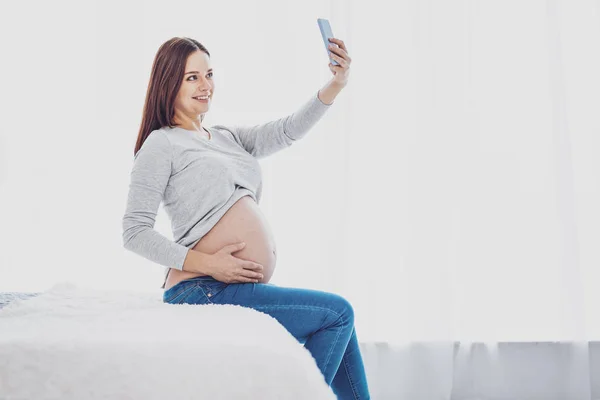 Encantadora mujer embarazada ocupada haciendo selfies — Foto de Stock