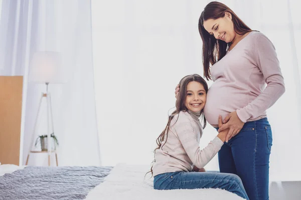 Positiv liten flicka att hålla hennes huvud på mödrar mage — Stockfoto