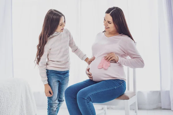 Glad gravid kvinna som visar lite strumpor till sin dotter — Stockfoto