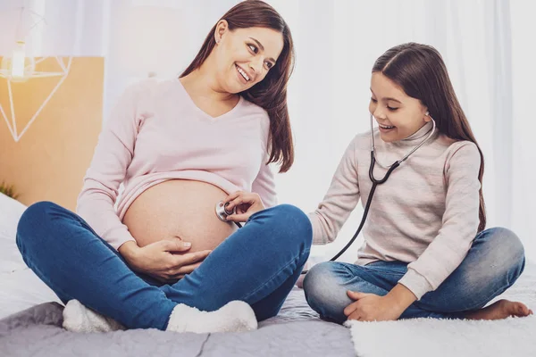 Toute la longueur de fille joyeuse enthousiaste écoutant son ventre de mères — Photo