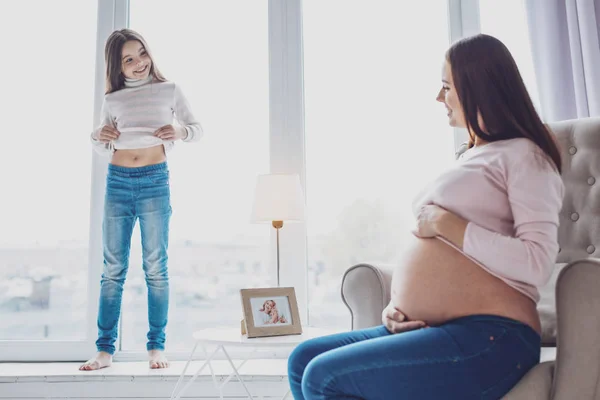 Zwangere moeder en haar dochtertje vergelijken hun magen — Stockfoto