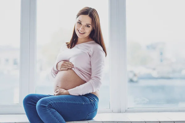 Charismatic young pregnant woman on window sill — Stock Photo, Image