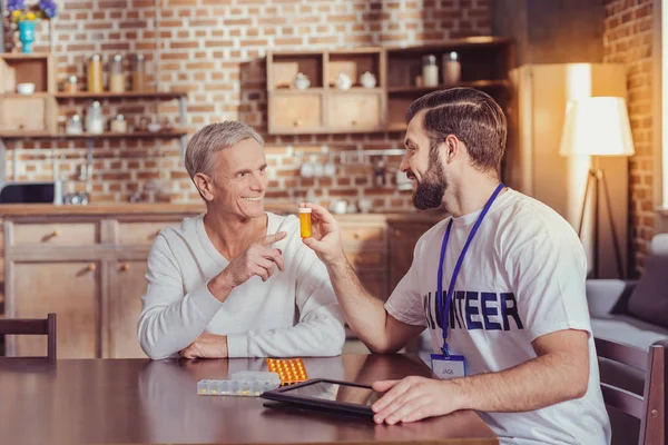 Behaglig grå mannen ler och pekar på piller. — Stockfoto