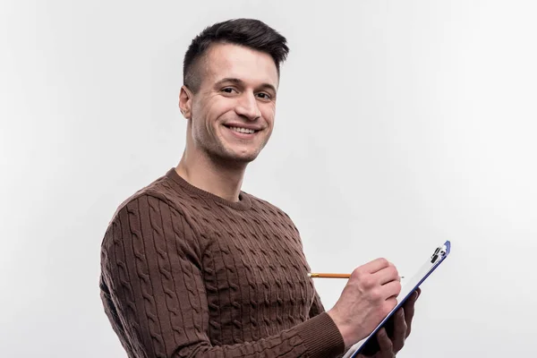 Sonriente secretaria masculina morena con suéter marrón haciendo notas —  Fotos de Stock
