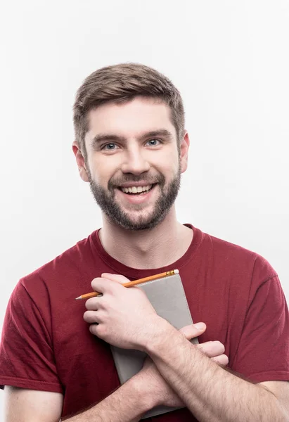 Piacevole studente barbuto sorridente che tiene quaderno e matita — Foto Stock