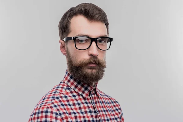 Hombre barbudo de pelo oscuro inteligente con gafas de pie cerca de la pared blanca — Foto de Stock