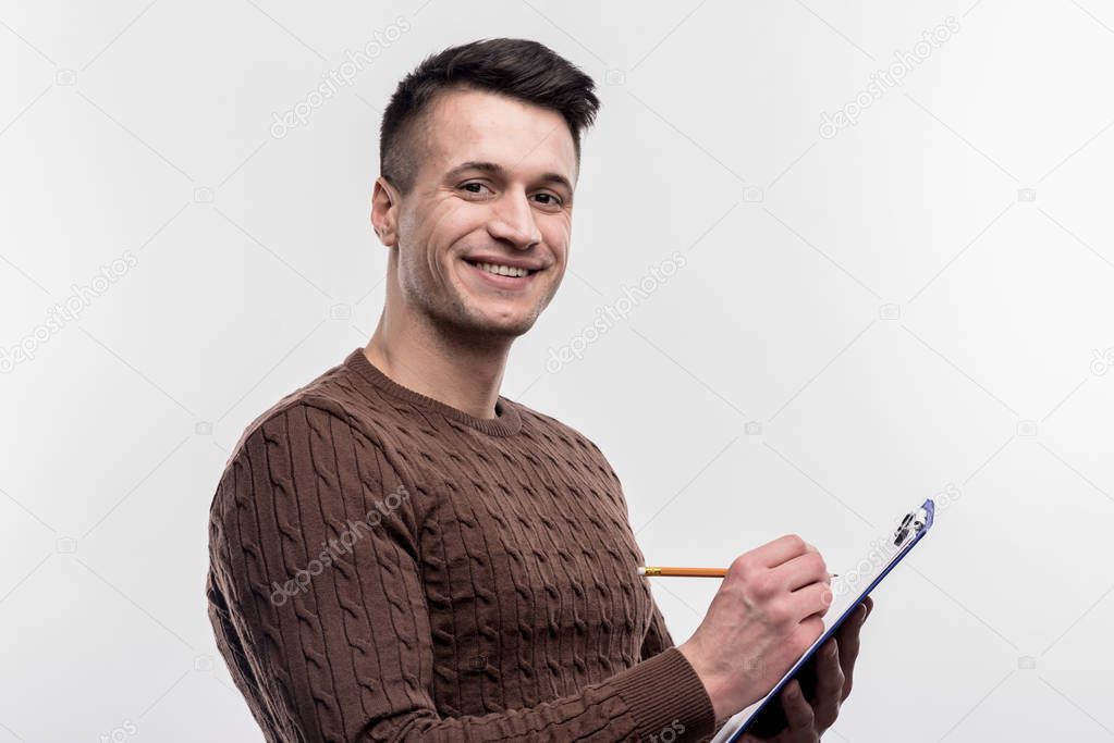 Smiling dark-haired male secretary wearing brown sweater making notes