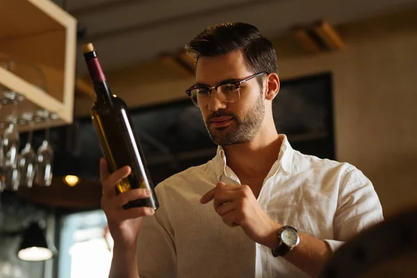 Inteligente bom homem olhando para a garrafa de vinho — Fotografia de Stock