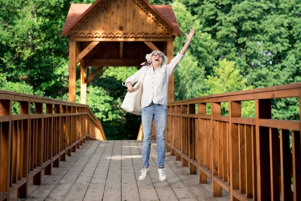 Happy retired woman jumping while enjoying nice eco tourism