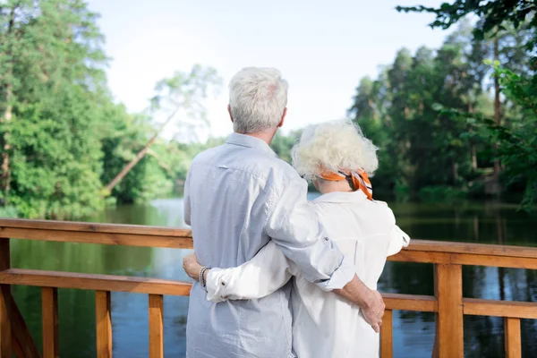 Casal de pensionistas abraçando uns aos outros olhando para o belo lago — Fotografia de Stock