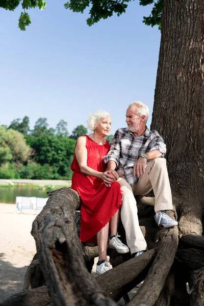 Linda pareja jubilada amorosa sentada en un gran árbol cerca del hermoso río — Foto de Stock