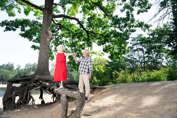 Idosa senhora vestindo vestido vermelho em pé na árvore perto de seu marido — Fotografia de Stock