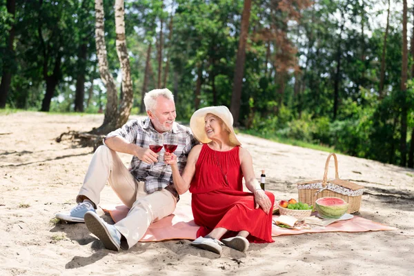 Aged couple clanging their glasses with red wine during picnic