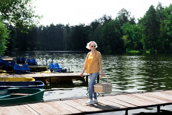 Mulher idosa usando óculos segurando cesto para piquenique na mão — Fotografia de Stock