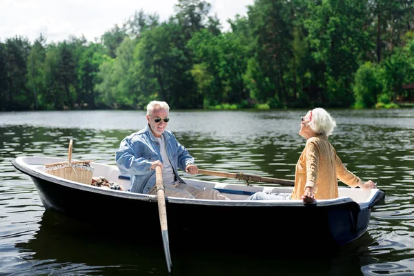 Happy elderly man holding paddles while sitting in boat with wife