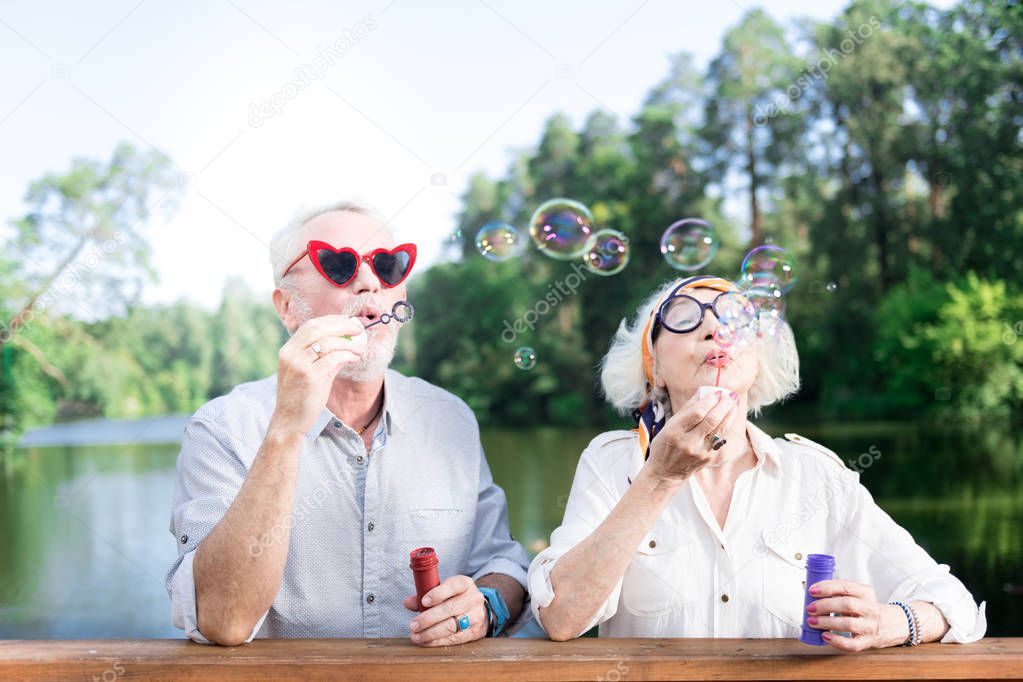 Grandfather and grandmother using soap bubbles of their grandchildren