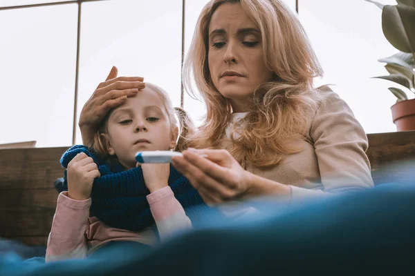 Cheerless young mother looking at the thermometer — Stock Photo, Image