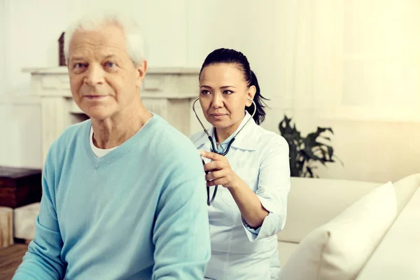 Profesional médico femenino escuchando los pulmones del hombre jubilado — Foto de Stock