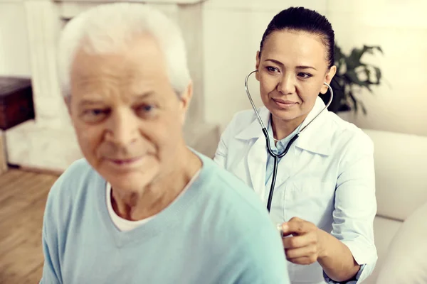 Mature female doctor listening to lungs of male patient