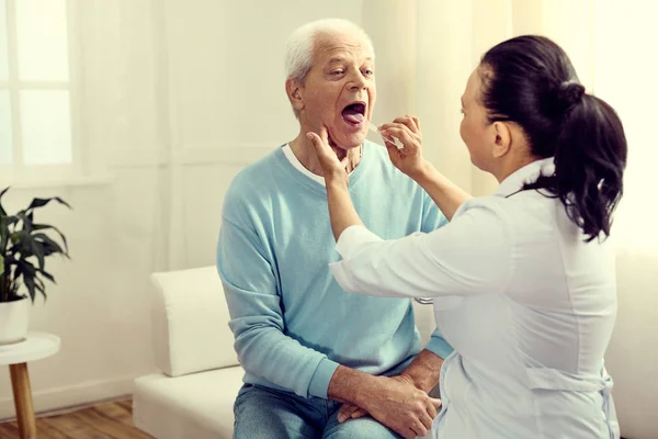 Médico de sexo femenino comprobando garganta de hombre mayor — Foto de Stock