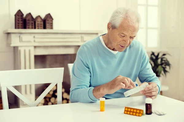 Uomo in pensione seduto a tavola e che prende farmaci — Foto Stock