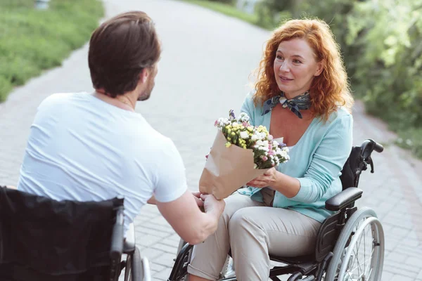 Mujer sorprendida en silla de ruedas recibiendo flores de novio — Foto de Stock