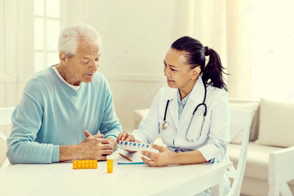 Female physician demonstrating elderly man weekly organizer