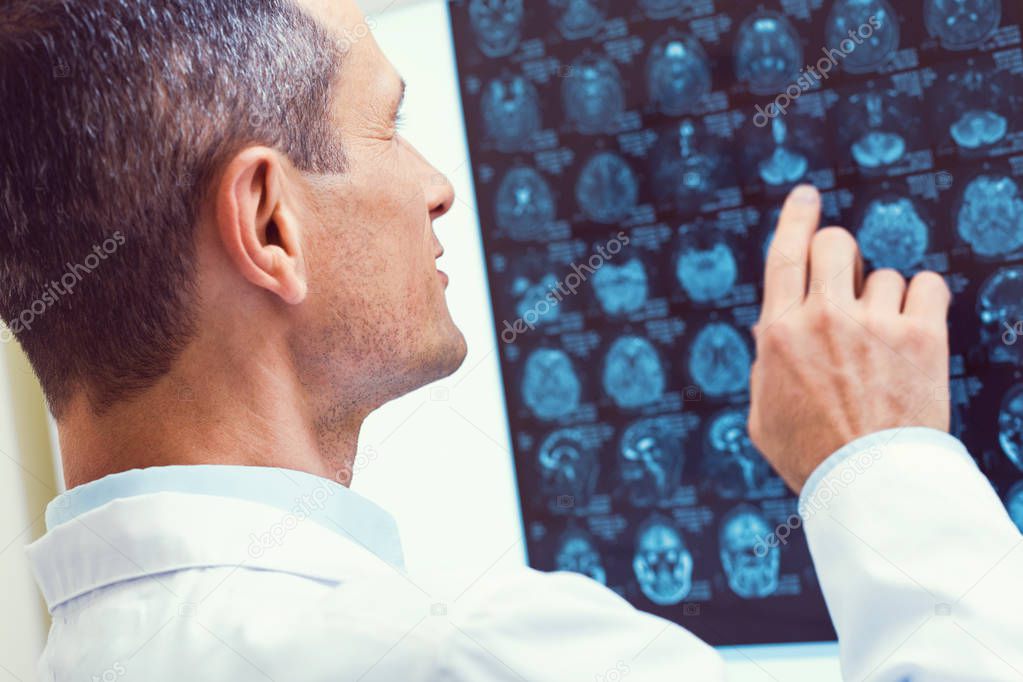 Let me check. Scaled up look on a turned back radiologist pointing toward a MRI scan while working in a lab and analyzing a brain scan.